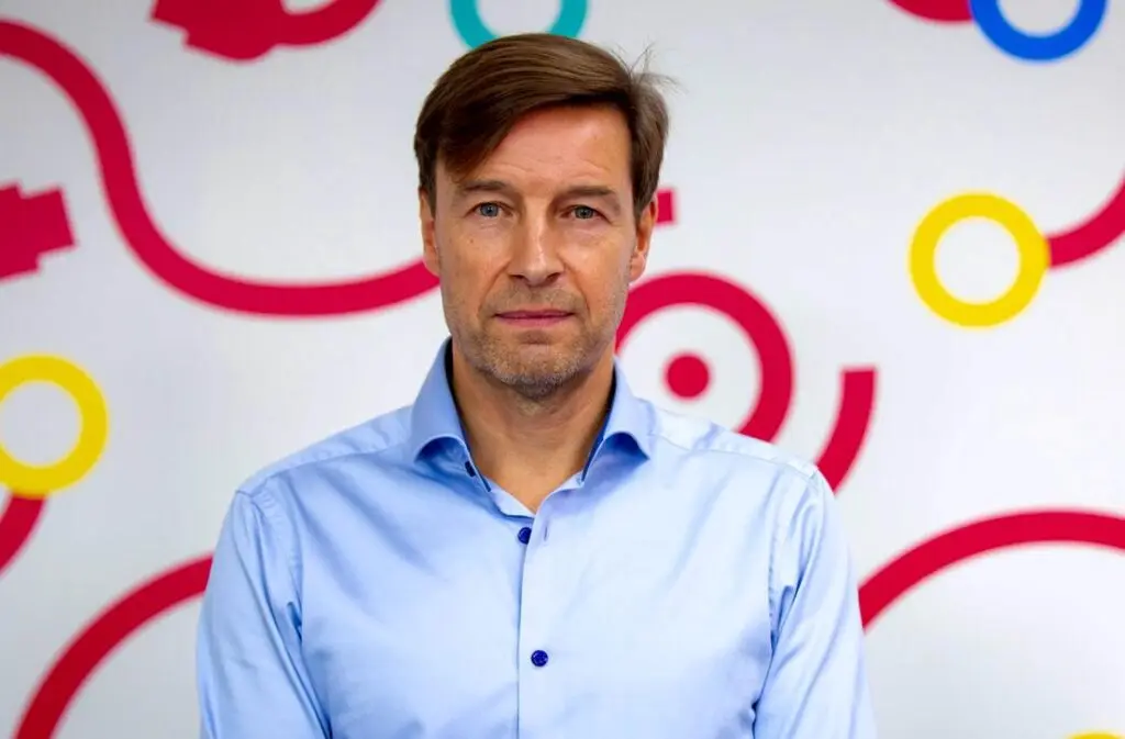 David Ritchie, Director or Propel Tech stands facing the camera, wearing a light blue button-up shirt, in front of a white wall decorated with colourful ring and swirl graphics in red, yellow, and blue